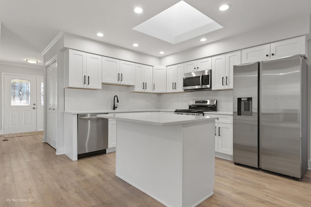 kitchen with sink, white cabinetry, a skylight, stainless steel appliances, and light hardwood / wood-style floors