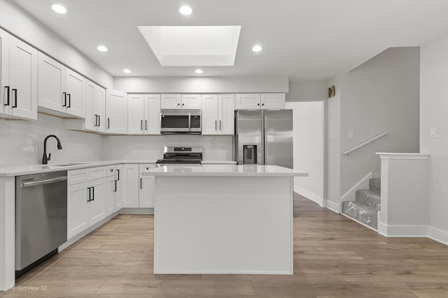 kitchen with sink, appliances with stainless steel finishes, white cabinetry, a skylight, and a kitchen island