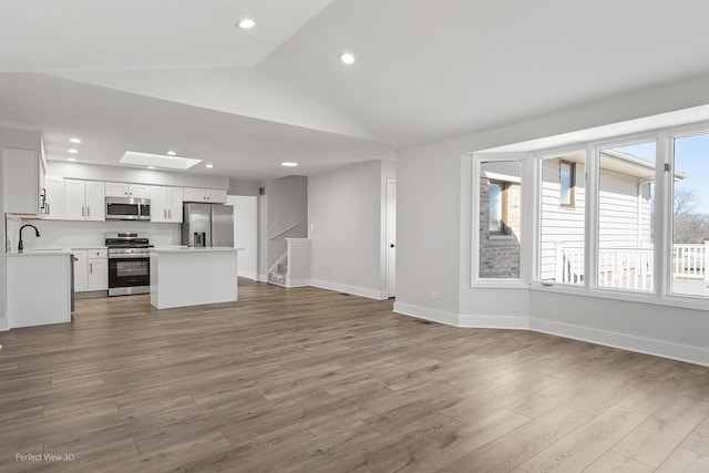 unfurnished living room featuring lofted ceiling with skylight and light hardwood / wood-style flooring