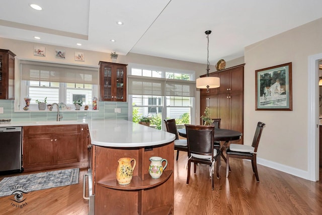 kitchen featuring pendant lighting, tasteful backsplash, sink, hardwood / wood-style flooring, and stainless steel dishwasher