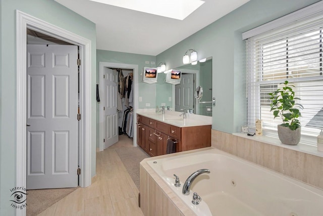 bathroom featuring a relaxing tiled tub, vanity, a skylight, and tile patterned floors