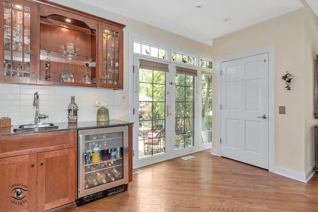 bar with sink, beverage cooler, backsplash, and light hardwood / wood-style flooring