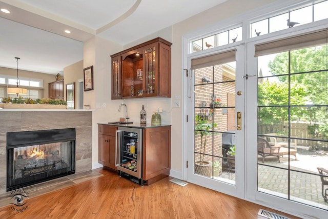 bar featuring wine cooler, a healthy amount of sunlight, decorative light fixtures, and light hardwood / wood-style flooring