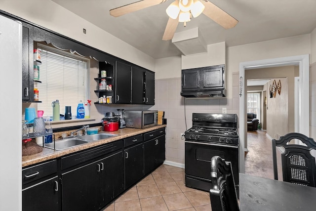 kitchen featuring light tile patterned flooring, sink, black gas range oven, ceiling fan, and decorative backsplash