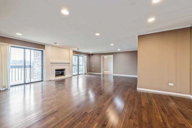 unfurnished living room with ornamental molding, wood finished floors, recessed lighting, baseboards, and a brick fireplace