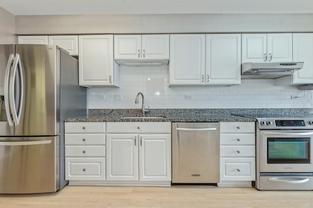 kitchen featuring under cabinet range hood, dark stone countertops, a sink, white cabinetry, and stainless steel appliances