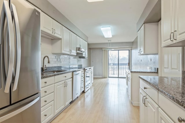 kitchen featuring stone counters, a sink, appliances with stainless steel finishes, light wood-type flooring, and backsplash