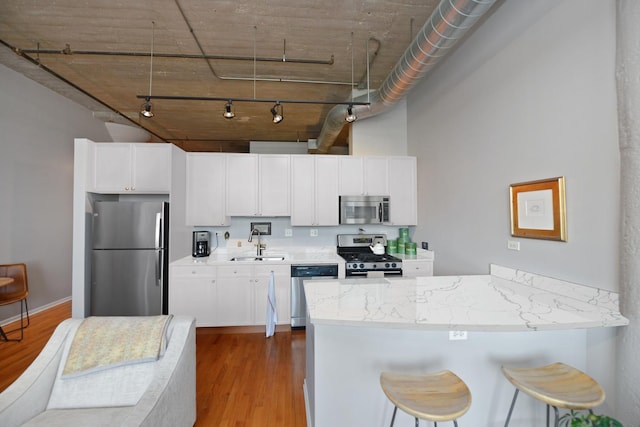 kitchen with sink, kitchen peninsula, stainless steel appliances, light hardwood / wood-style floors, and white cabinets