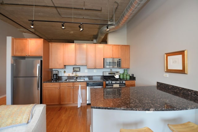 kitchen featuring sink, dark stone countertops, a kitchen bar, stainless steel appliances, and light hardwood / wood-style flooring