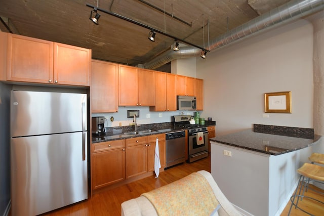 kitchen with appliances with stainless steel finishes, kitchen peninsula, light wood-type flooring, and dark stone countertops