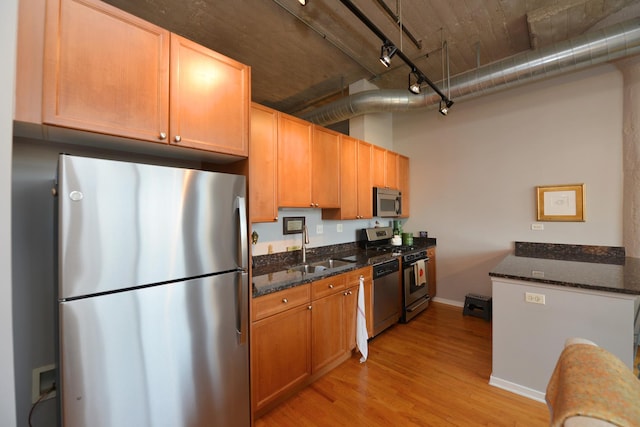 kitchen featuring appliances with stainless steel finishes, sink, light hardwood / wood-style flooring, and dark stone counters