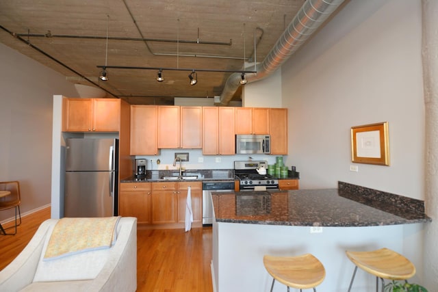 kitchen featuring sink, dark stone countertops, kitchen peninsula, stainless steel appliances, and light wood-type flooring