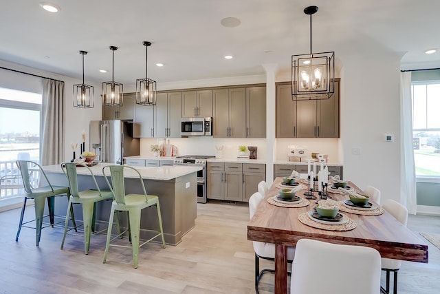 kitchen with appliances with stainless steel finishes, light stone countertops, a kitchen island with sink, and hanging light fixtures