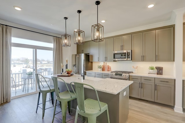 kitchen with light stone counters, hanging light fixtures, an island with sink, and appliances with stainless steel finishes