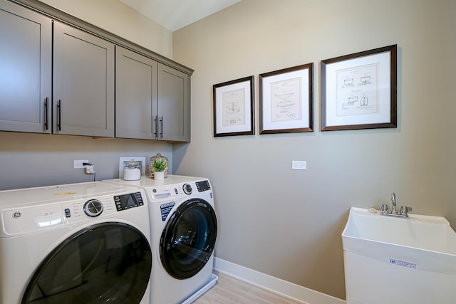 laundry area featuring sink, washer and clothes dryer, light hardwood / wood-style floors, and cabinets