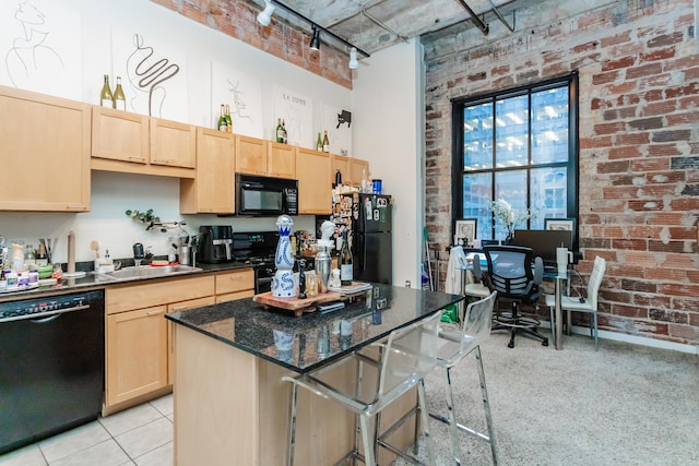 kitchen with brick wall, a high ceiling, a center island, black appliances, and light brown cabinets