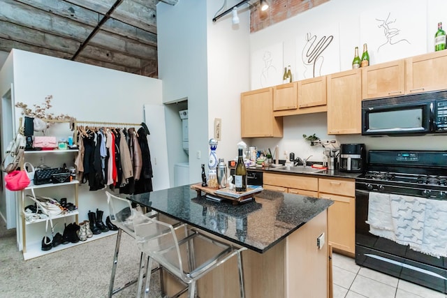 kitchen featuring a towering ceiling, sink, dark stone counters, black appliances, and light brown cabinets