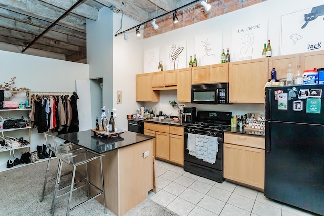 kitchen featuring light brown cabinetry, black appliances, a breakfast bar, and a high ceiling