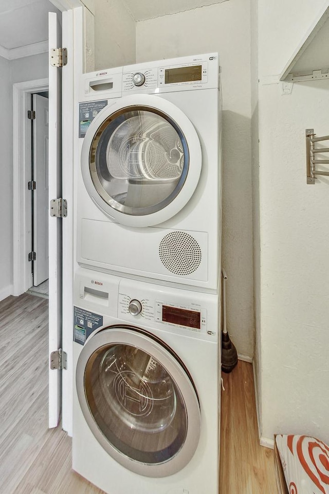 laundry room featuring stacked washer / drying machine, crown molding, and light hardwood / wood-style flooring