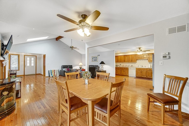 dining space featuring ceiling fan, lofted ceiling with skylight, sink, and light wood-type flooring