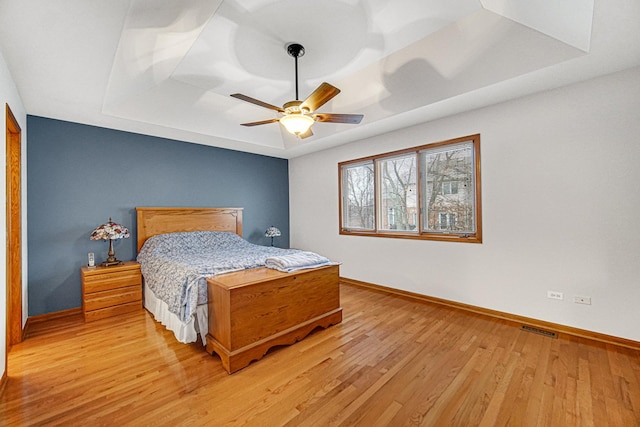 bedroom with a tray ceiling, light hardwood / wood-style flooring, and ceiling fan