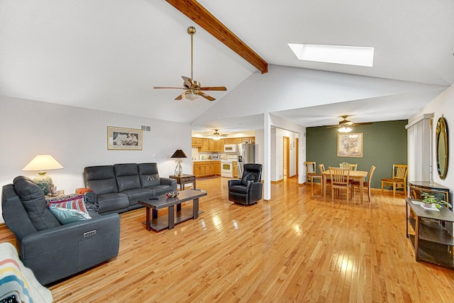 living room featuring ceiling fan, beam ceiling, a skylight, high vaulted ceiling, and light wood-type flooring