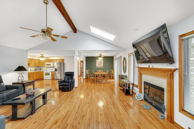 living room with vaulted ceiling with skylight, a tiled fireplace, and light hardwood / wood-style floors