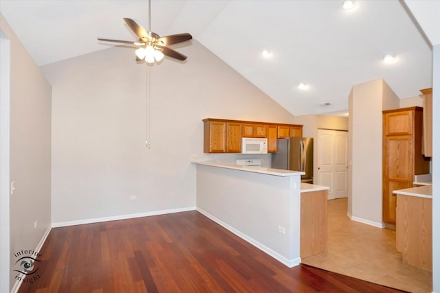 kitchen with wood-type flooring, ceiling fan, stainless steel fridge, kitchen peninsula, and high vaulted ceiling