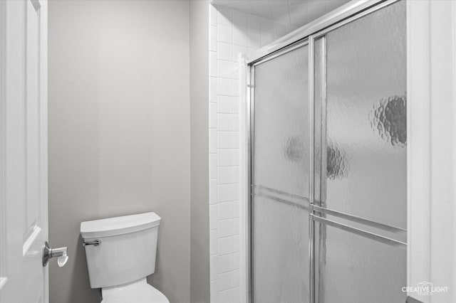 bathroom featuring toilet and a shower with shower door