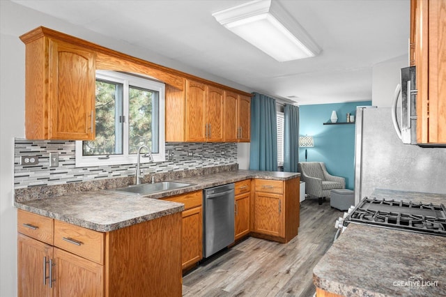 kitchen with stainless steel appliances, sink, decorative backsplash, and light wood-type flooring