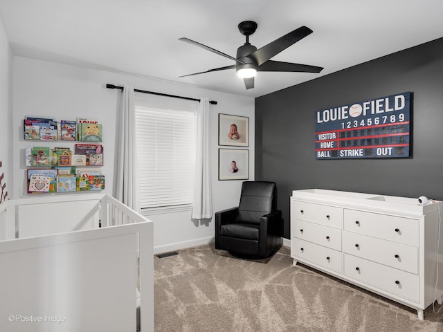 bedroom featuring light colored carpet, ceiling fan, a crib, and baseboards