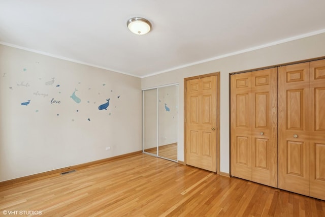 unfurnished bedroom featuring hardwood / wood-style floors, ornamental molding, and multiple closets