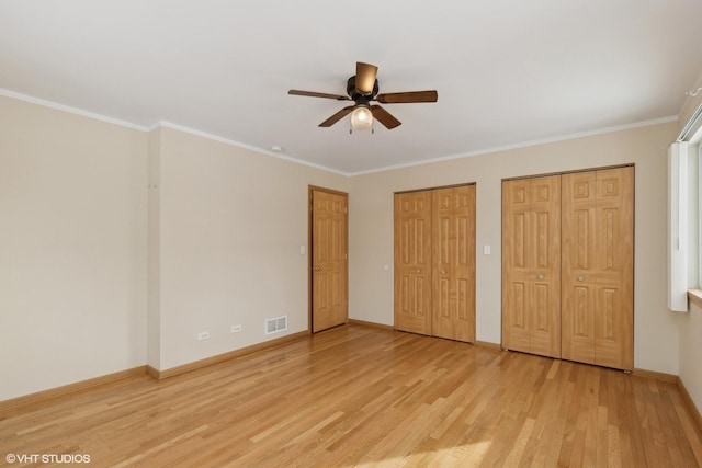 unfurnished bedroom with multiple closets, ceiling fan, crown molding, and light hardwood / wood-style flooring