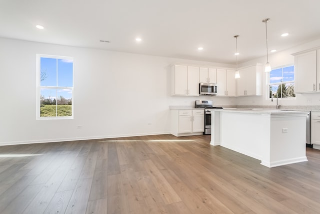 kitchen with light hardwood / wood-style flooring, white cabinetry, stainless steel appliances, a kitchen island, and decorative light fixtures