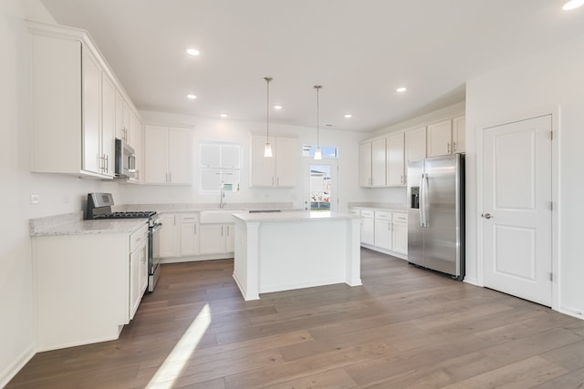 kitchen with sink, white cabinetry, decorative light fixtures, appliances with stainless steel finishes, and a kitchen island