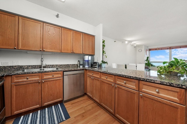 kitchen with light wood finished floors, dark stone counters, brown cabinetry, dishwasher, and a sink