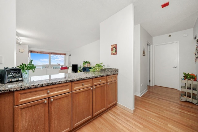 kitchen featuring dark stone counters, brown cabinets, light wood-style flooring, and baseboards