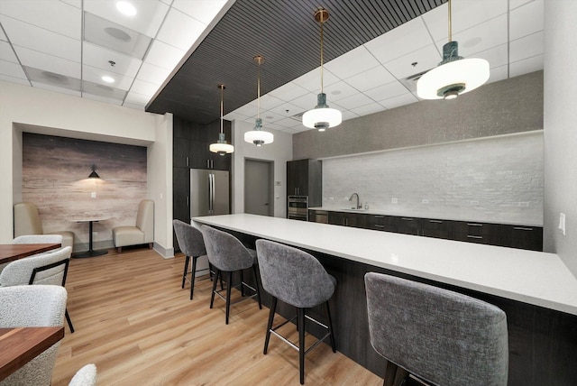 kitchen featuring dark cabinets, a sink, light countertops, stainless steel refrigerator, and light wood finished floors