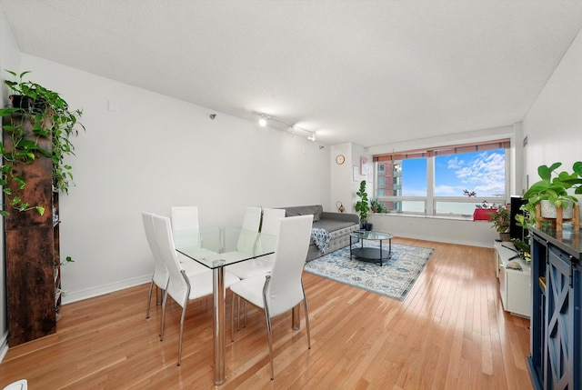 dining space with baseboards, a textured ceiling, and light wood-style floors