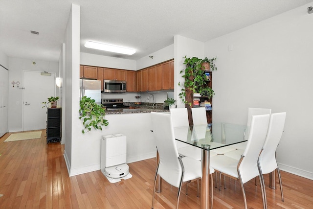 kitchen with light wood-style flooring, appliances with stainless steel finishes, brown cabinets, and a textured ceiling