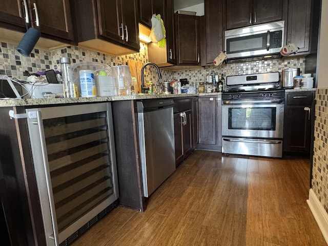 kitchen featuring dark wood-type flooring, appliances with stainless steel finishes, wine cooler, light stone counters, and decorative backsplash