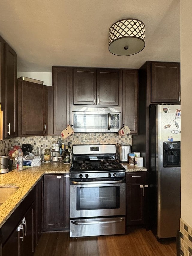 kitchen featuring appliances with stainless steel finishes, dark hardwood / wood-style floors, light stone countertops, and decorative backsplash