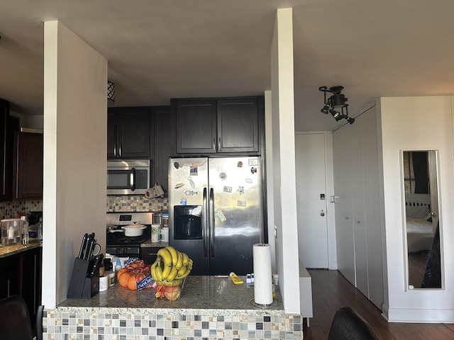 kitchen featuring appliances with stainless steel finishes, dark hardwood / wood-style flooring, stone countertops, and backsplash