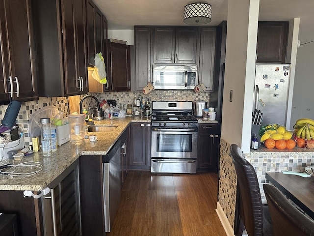 kitchen with dark brown cabinetry, sink, light stone counters, appliances with stainless steel finishes, and dark hardwood / wood-style flooring