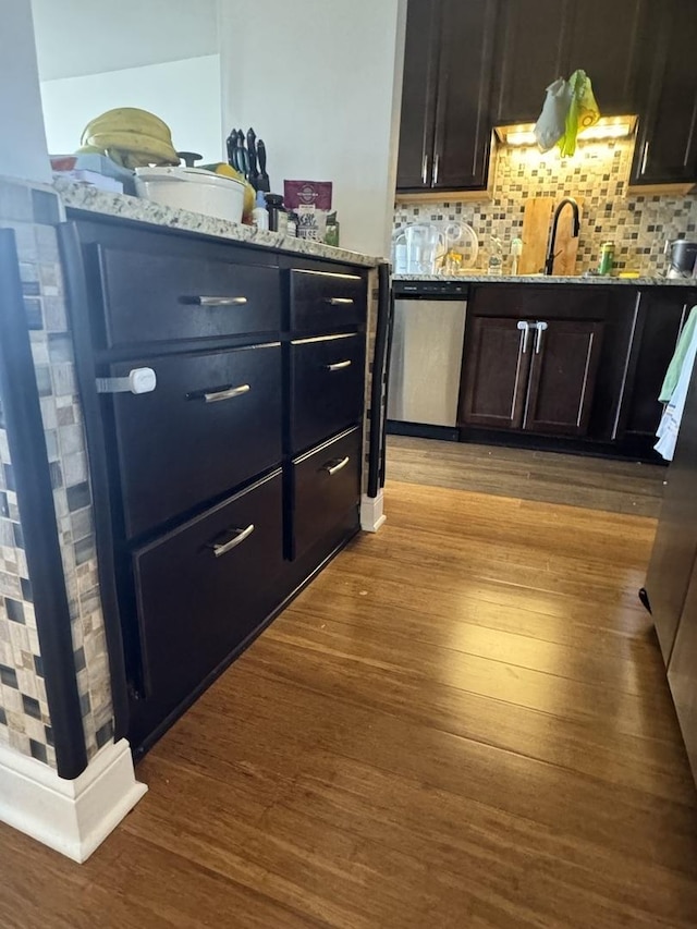 bar featuring tasteful backsplash, dishwasher, sink, light stone countertops, and light wood-type flooring