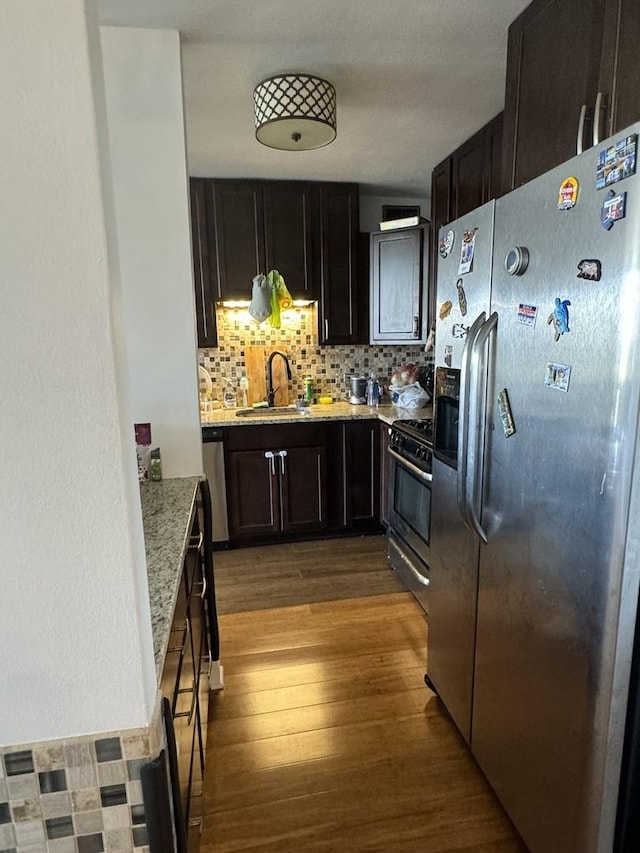 kitchen with sink, tasteful backsplash, stainless steel appliances, light stone countertops, and light hardwood / wood-style floors