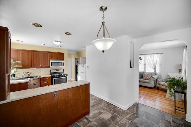 kitchen featuring sink, appliances with stainless steel finishes, light stone countertops, decorative backsplash, and decorative light fixtures