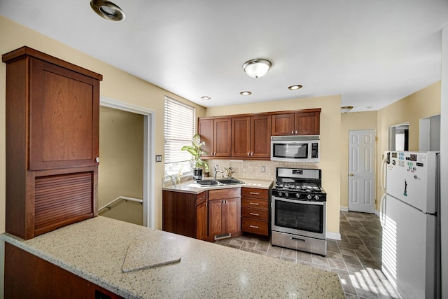 kitchen with appliances with stainless steel finishes, sink, light stone counters, and decorative backsplash