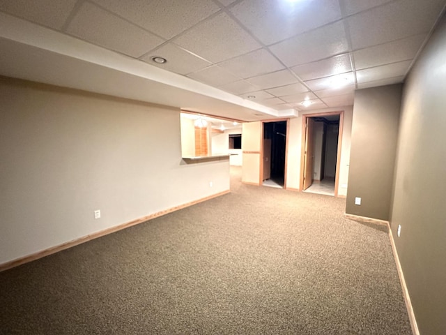 finished basement with baseboards, a drop ceiling, and carpet flooring