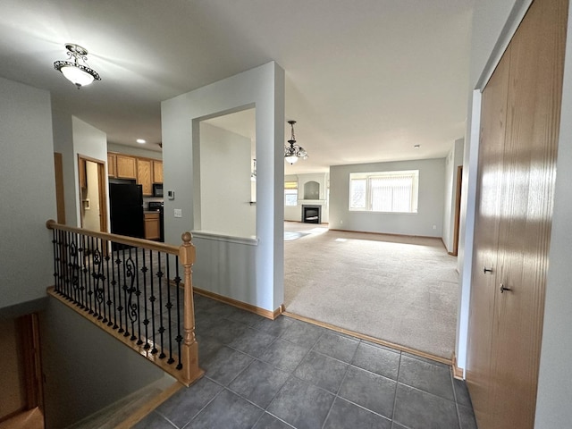 corridor featuring dark tile patterned floors, baseboards, dark colored carpet, and an upstairs landing